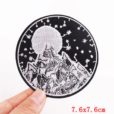Circular patch with mountain and moon design held by a hand, on a white background
