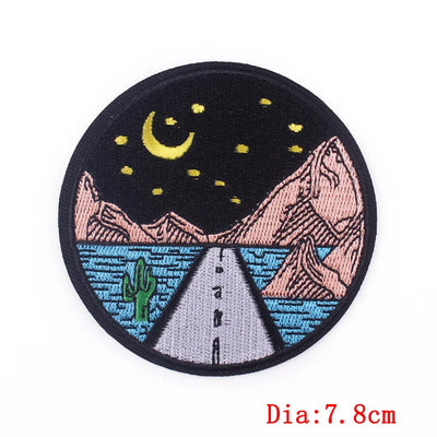 Round embroidered patch with a desert landscape design featuring mountains, a road, and cacti under a night sky with a moon and stars.