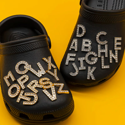 Black clogs with rhinestone letters shoe charms on a yellow background