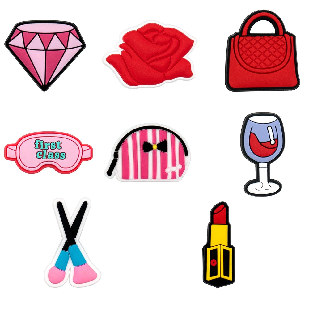 Set of colorful shoe charms including a diamond, rose, handbag, sleep mask, makeup bag, glass, and lipstick on a white background.