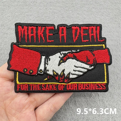 Embroidered patch with handshake design and text 'Make a Deal for the Sake of Our Business' held by a hand on a gray background.