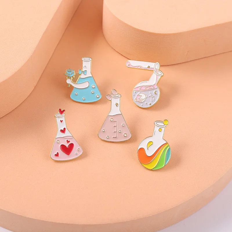 Set of colorful science-themed enamel pins on a peach-colored stand.