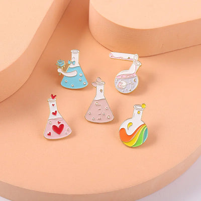 Set of colorful science-themed enamel pins on a peach-colored stand.