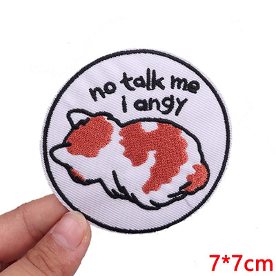 Circular patch with a cat illustration and text 'no talk me I angy' held by a hand on a white background.