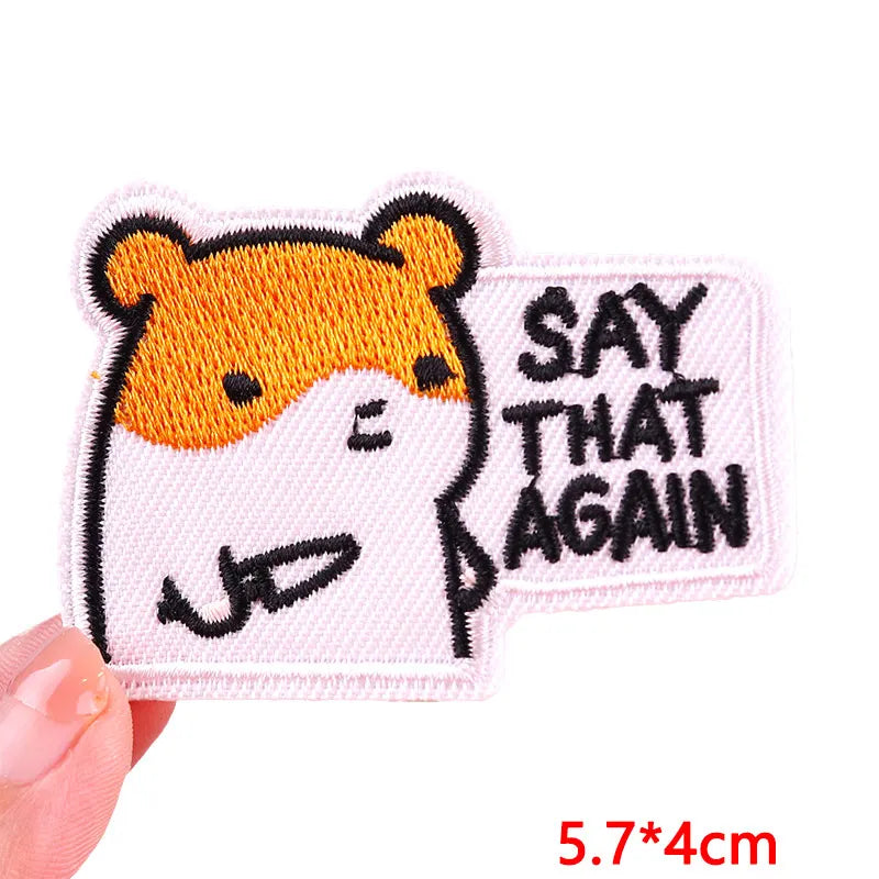 Embroidered patch with a cartoon hamster and text 'SAY THAT AGAIN' held by a hand.