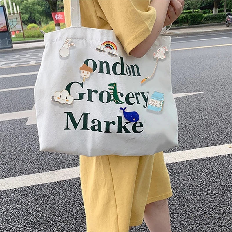 Person holding a white tote bag with decorative elements and text on a street.