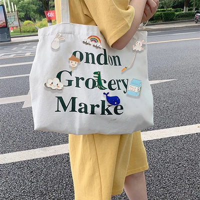 Person holding a white tote bag with decorative elements and text on a street.