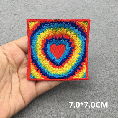 Colorful embroidered patch with a heart design held by a hand on a gray background