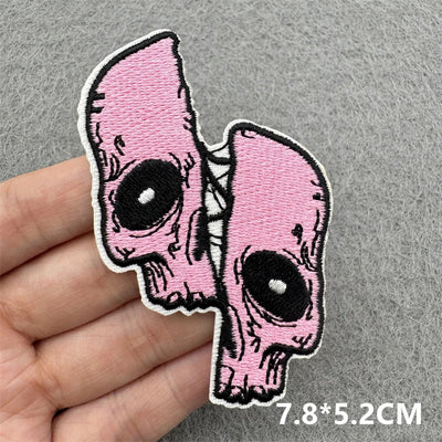 Pink skull-shaped patch held by a hand on a gray background