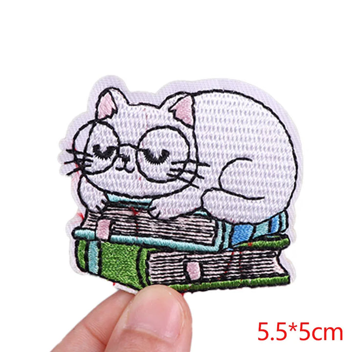 Embroidered patch of a cat reading a book held by a hand on a white background