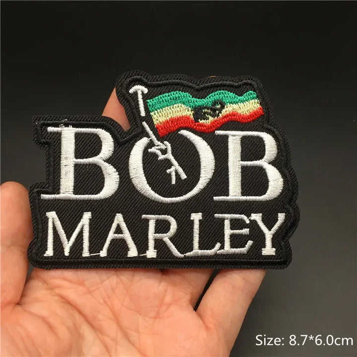 Hand holding a Bob Marley reggae with Rastafarian flag embroidered iron-on patch 8.7x6cm on a dark background