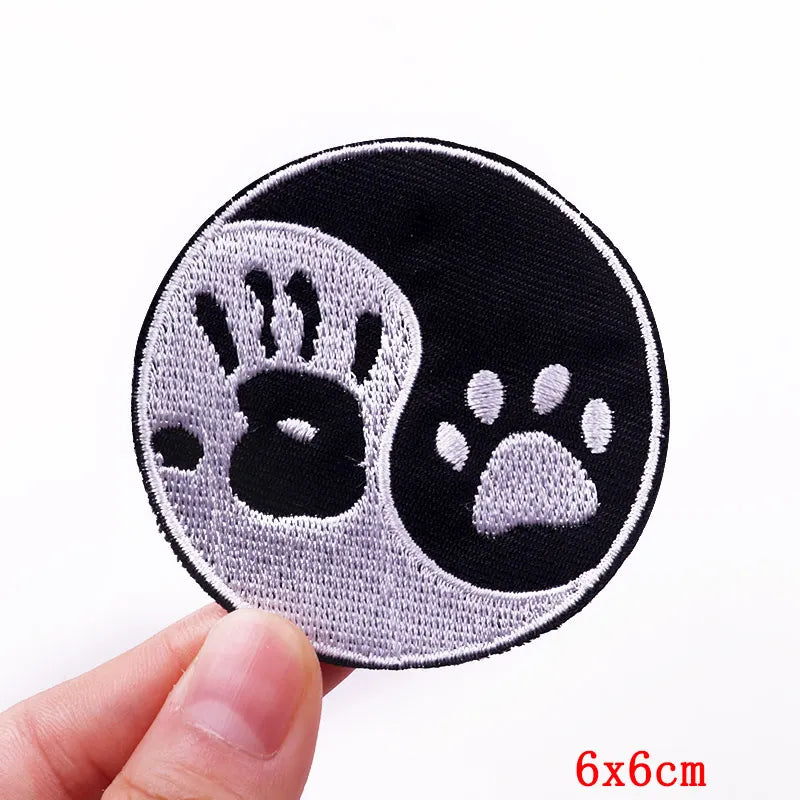 Circular patch with black and white paw prints held by a hand on a white background