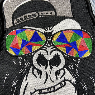 Embroidered patch of a skeleton wearing colorful sunglasses and a cap on a black background
