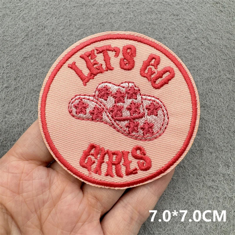 Pink patch with 'Let's Go Girls' text and flip-flop design held by a hand on a gray background.