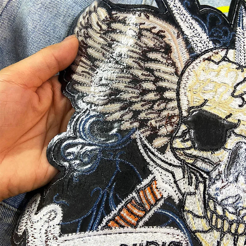 Hand holding a patch with intricate designs and text on a denim fabric background.