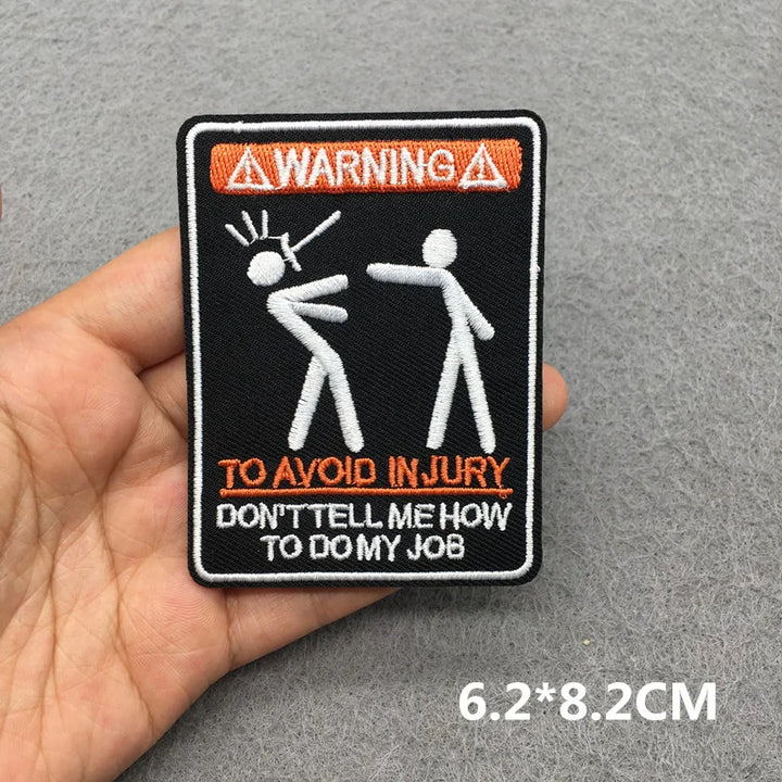 Patch with stick figures and text held by a hand on a gray background
