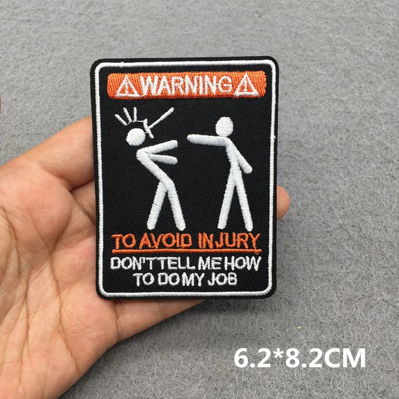 Patch with stick figures and text held by a hand on a gray background