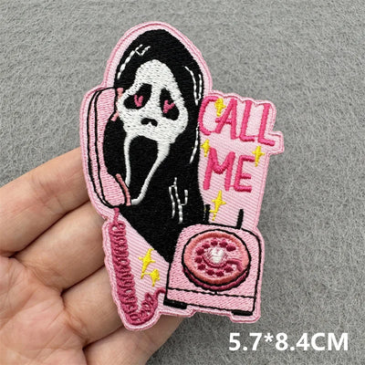 Embroidered patch with a ghost face design and 'Call Me' text held by a hand on a gray background.