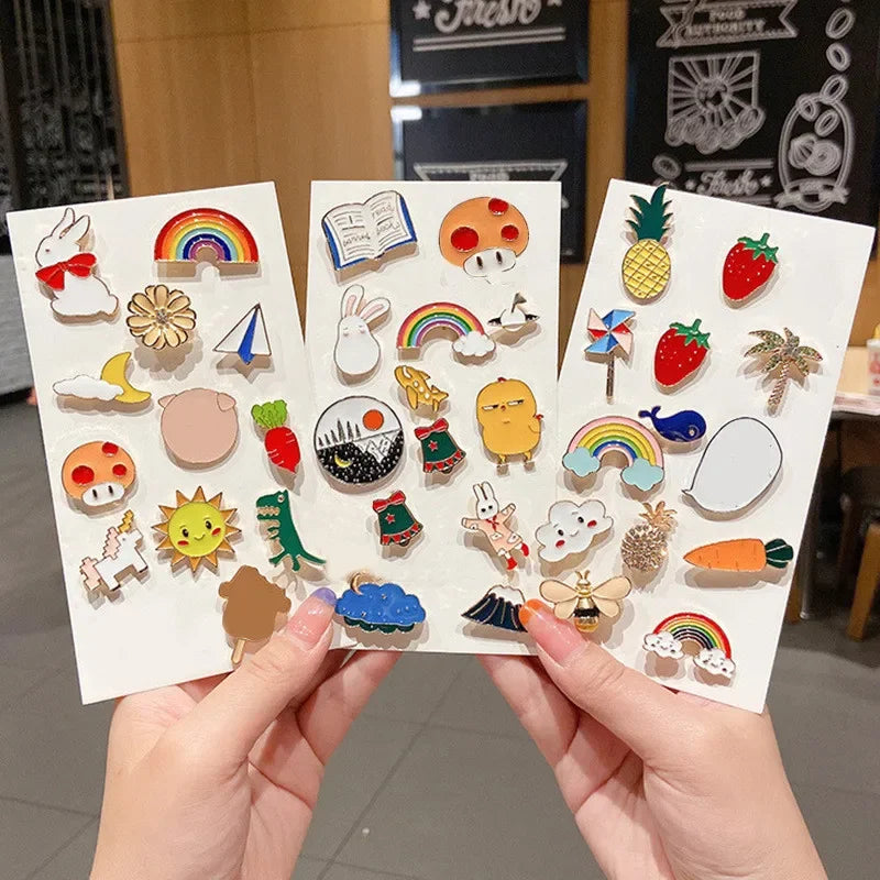 Three sheets of colorful enamel pins held by hands with a blurred indoor background.