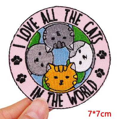 Circular patch with cartoon cats and text 'I love all the cats in the world' held by a hand.