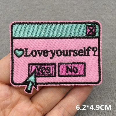 Pink patch with 'Love yourself?' question and 'Yes'/'No' options held in a hand against a gray background.