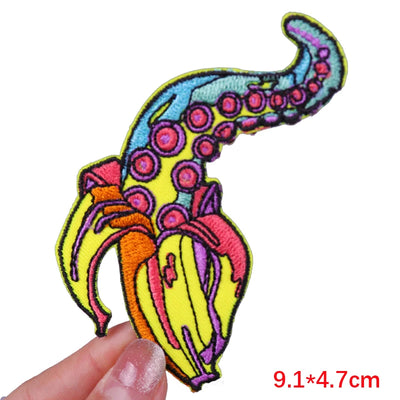Colorful embroidered patch of a banana with octopus tentacles held by a hand on a white background.