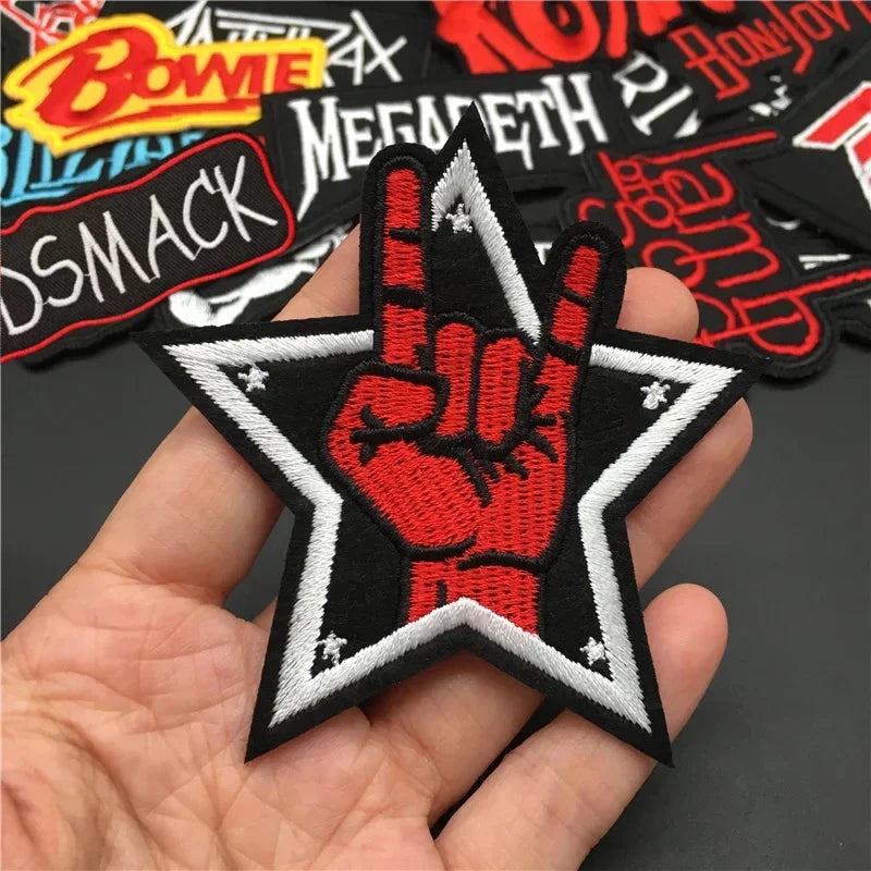 Hand holding a patch with a red hand and star design, surrounded by other patches on a dark background.