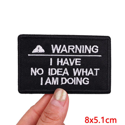 Black patch with white text 'WARNING I HAVE NO IDEA WHAT I AM DOING' held by a hand.