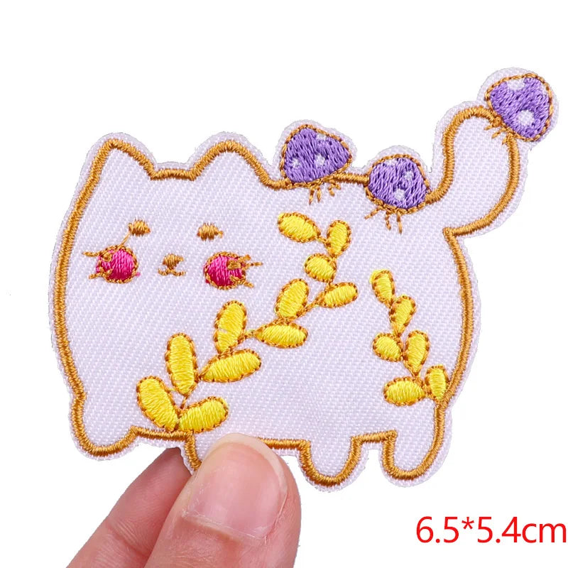 Embroidered patch of a cat with flowers held by a hand, on a white background.