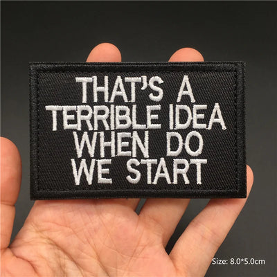 Black patch with white text held in a hand against a dark background