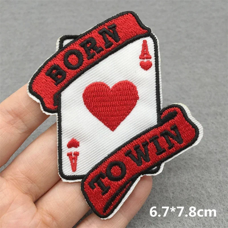 Embroidered patch with 'Born to Win' text and heart design held by a hand on a gray background.