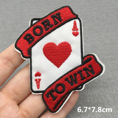 Embroidered patch with 'Born to Win' text and heart design held by a hand on a gray background.