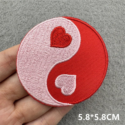 Circular patch with yin yang design featuring hearts held by a hand on a gray background.