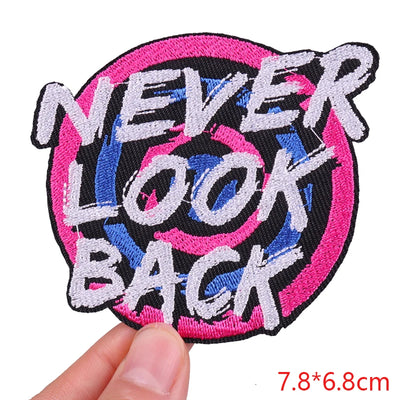 Embroidered patch with 'NEVER LOOK BACK' text held by a hand on a white background
