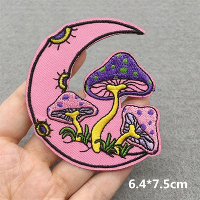 Pink embroidered patch with mushrooms and a moon held by a hand on a gray background