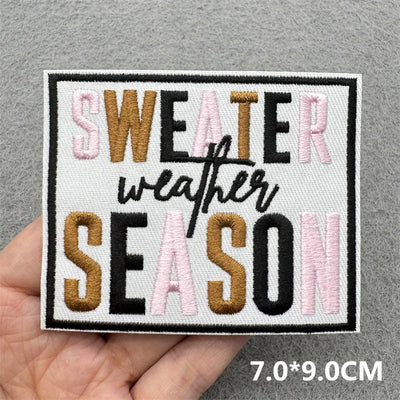 Embroidered patch with 'SWEATER weather SEASON' text held by a hand on a gray background.