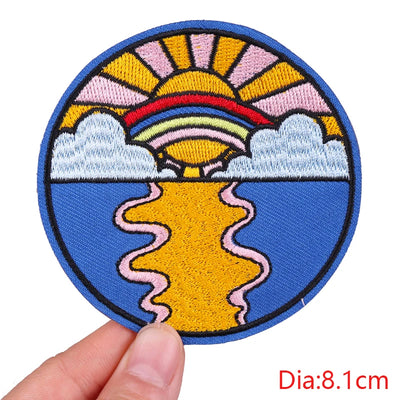 Circular embroidered patch with a colorful design of a sun and clouds held by a hand on a white background.