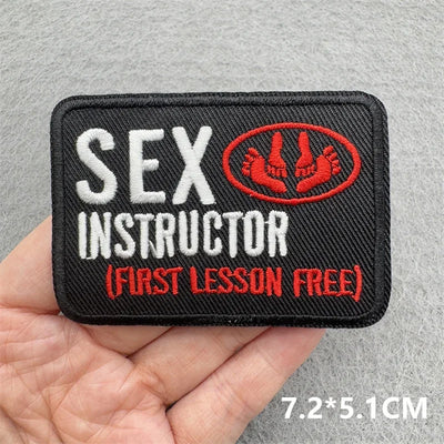 Embroidered patch with 'Sex Instructor' text held in a hand on a gray background