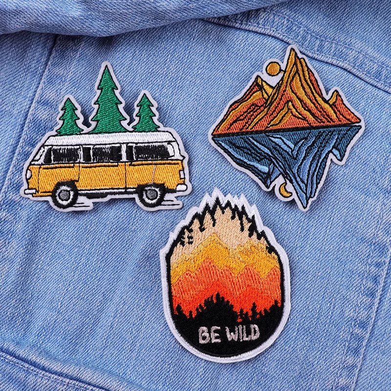 Three embroidered patches on a denim jacket: a van, mountains, and 'BE WILD' design.