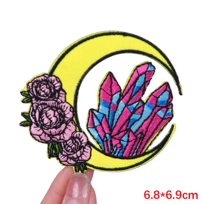 Embroidered patch with flowers and crystals on a yellow crescent moon, held by a hand.