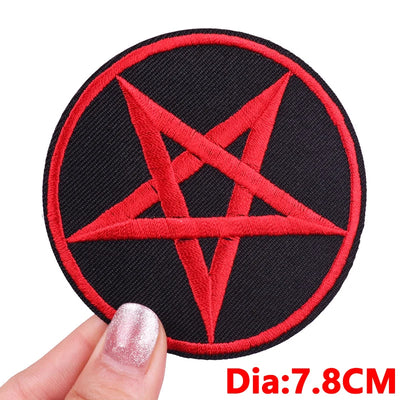 Red pentagram patch on black background held by a hand with red nail polish.