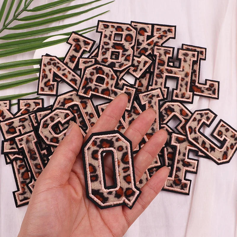 Leopard print letter patches on a white background with a hand holding a patch.