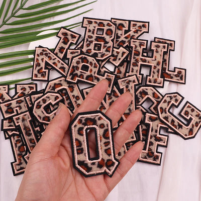 Leopard print letter patches on a white background with a hand holding a patch.