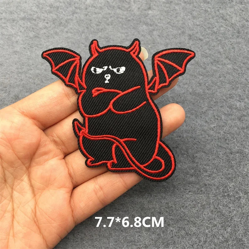 Black and red bat-shaped patch held in a hand with a gray background