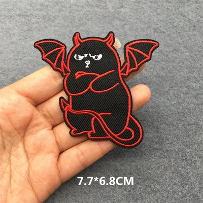 Black and red bat-shaped patch held in a hand with a gray background