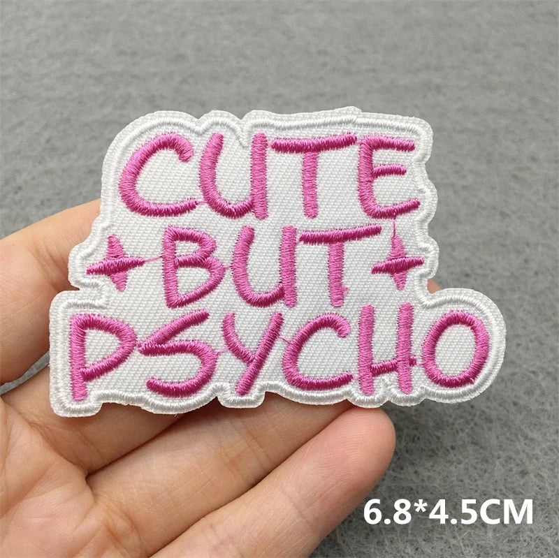 Embroidered patch with 'CUTE BUT PSYCHO' text held by a hand on a gray background