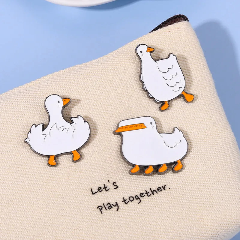 Three cartoon duck pins on a beige surface with &