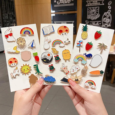 Three sheets of colorful enamel pins held by hands with a blurred background
