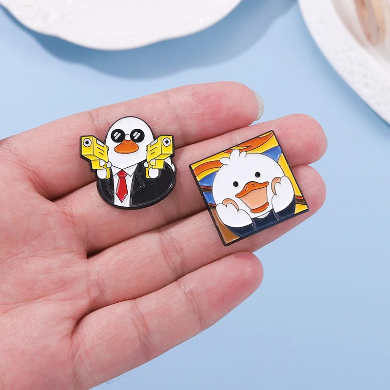 Two cartoon duck pins held in a hand against a light blue background