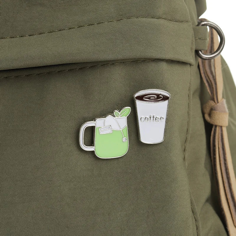 Two pins on a green backpack: one resembling a green drink with a straw and the other a coffee cup.